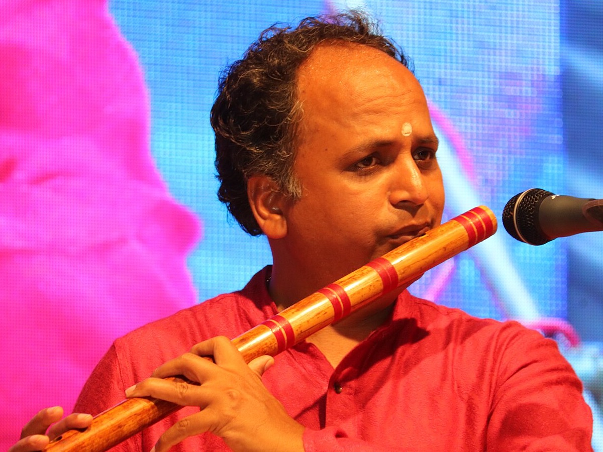Player sounding a bansuri tone: lips at the blowing hole, flute supported, fingers ready