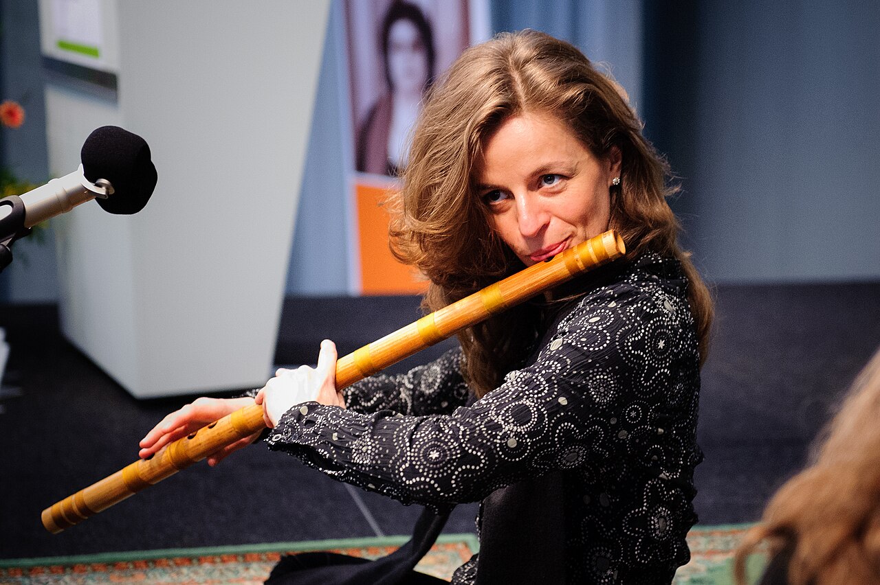Musician sitting upright with a side-blown bansuri extending to the right